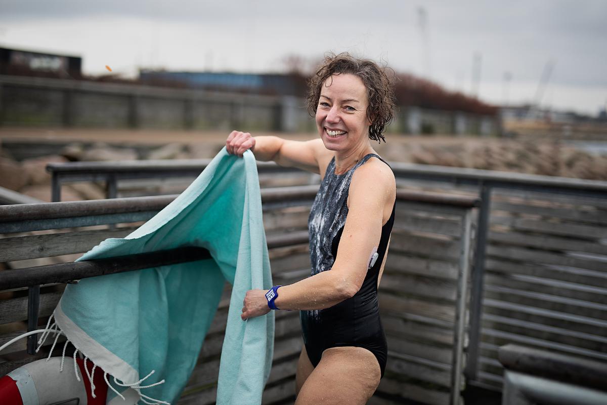 Billede af smilende kvinde i badedragt. Hun har en sensor på venstre overarm.