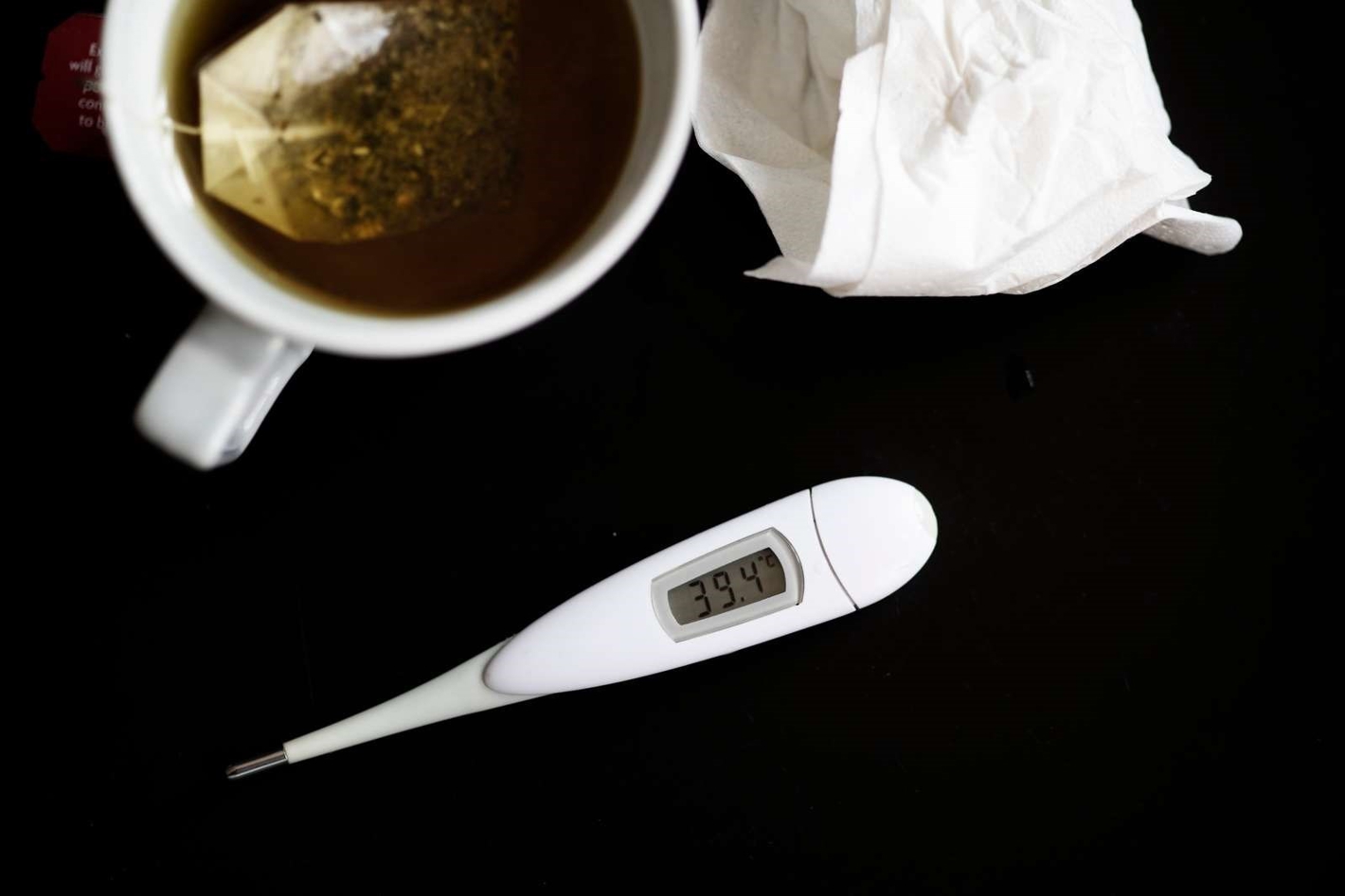 Billede af et termometer, papirlommetørklæde og en kop te på et bord.