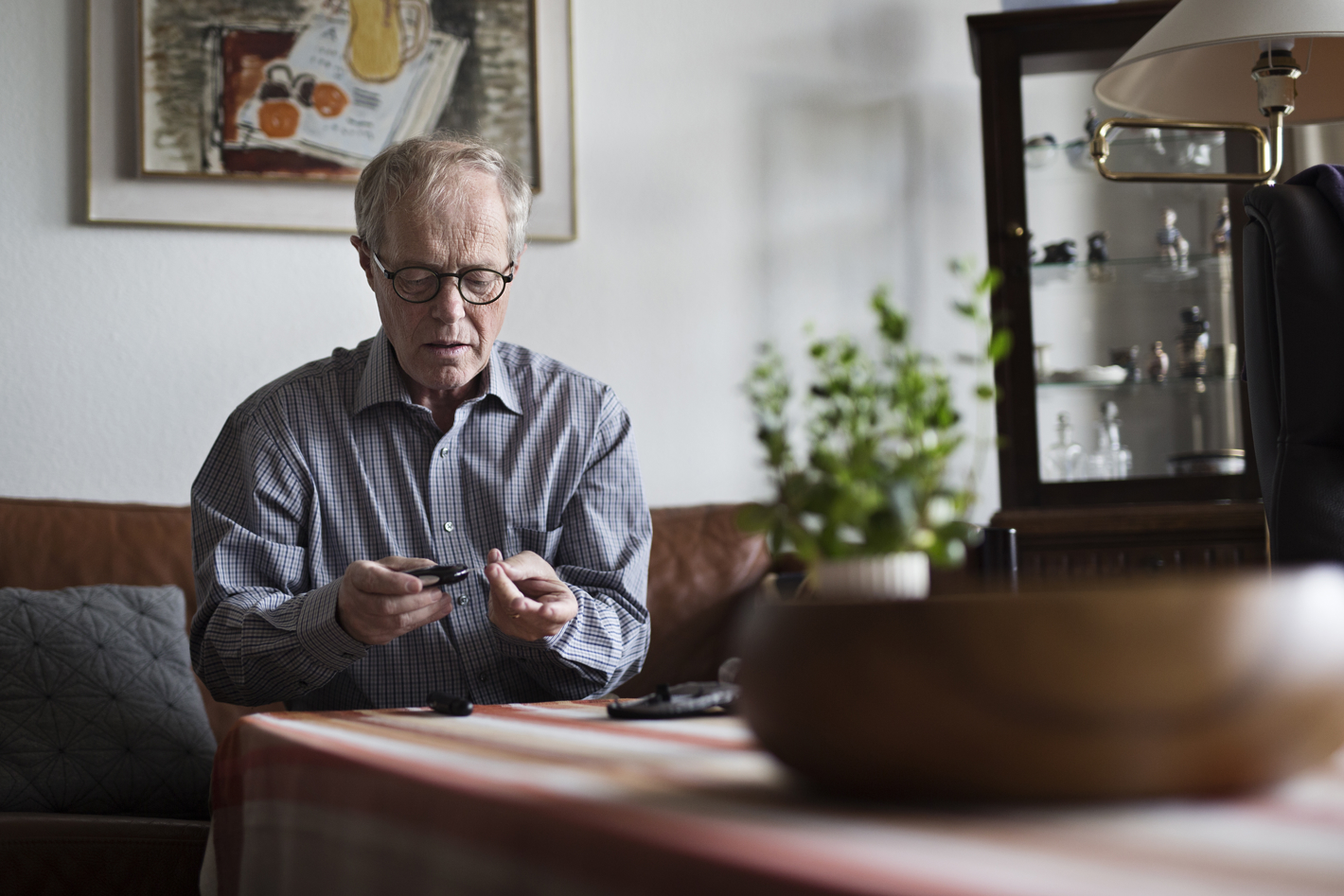 En ældre mand med diabetes, der sidder i sin stue og måler blodsukker.