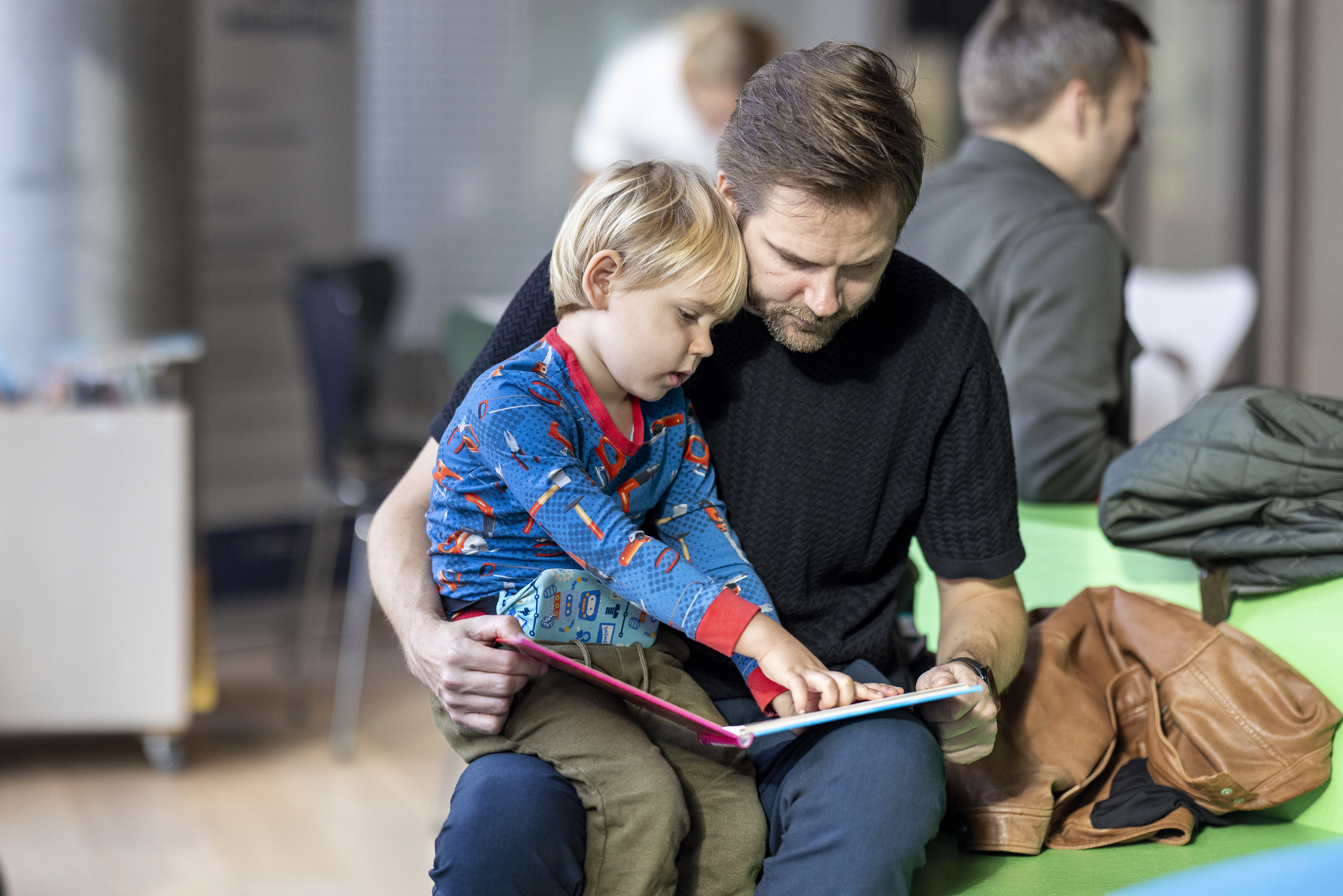 Billede af en far, der sidder med et lille barn på skødet og læser i en billedbog.