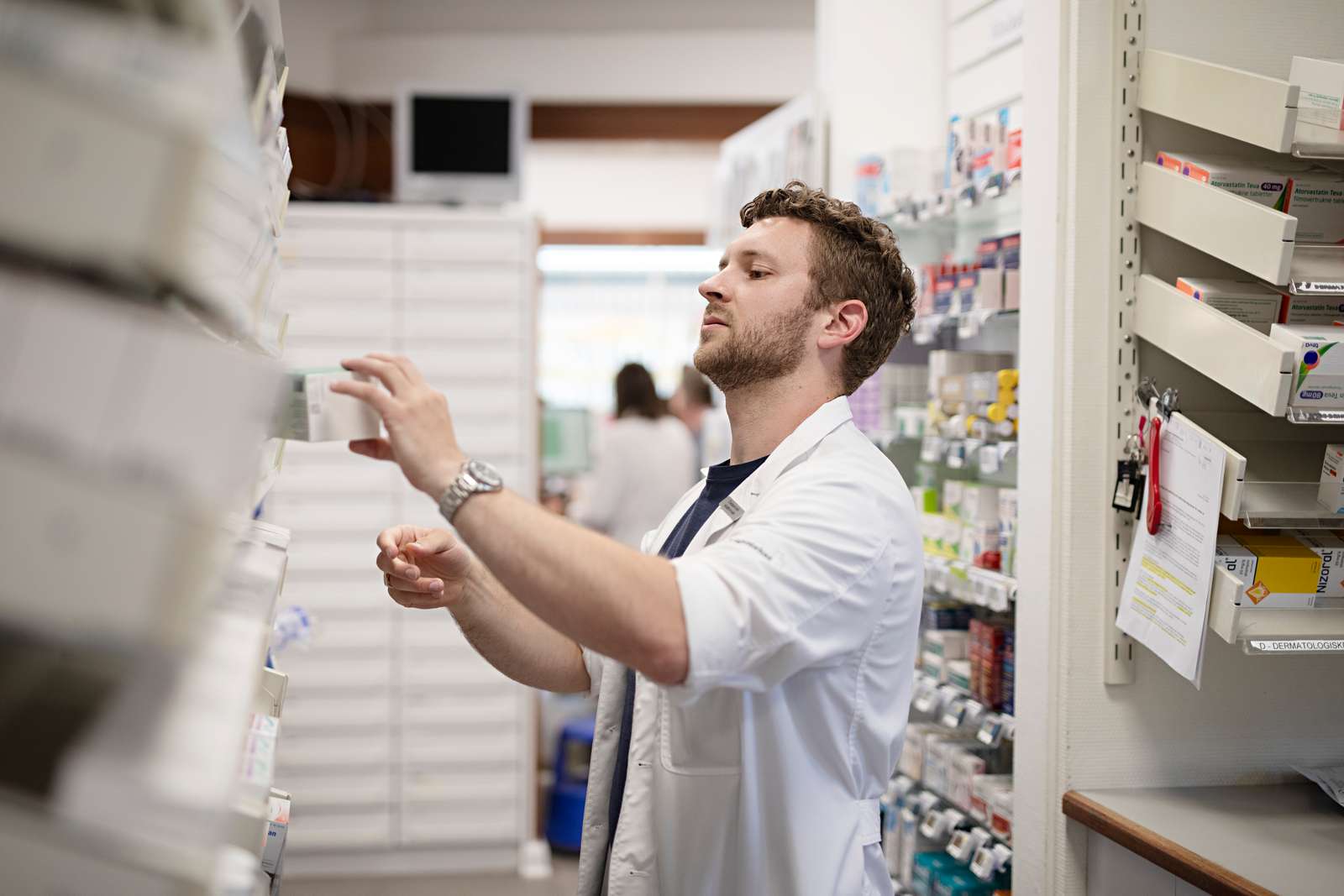 Mandlig apoteker står ved medicinhylde og tager en æske medicin ned